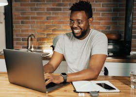 African American man smiling while working remotely on laptop from home office
