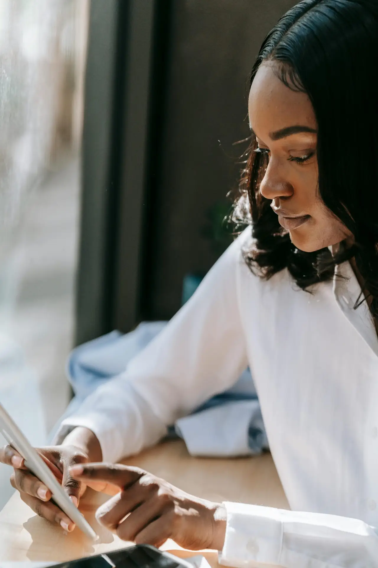 Focused woman in casual setting interacting with her smartphone near window light.